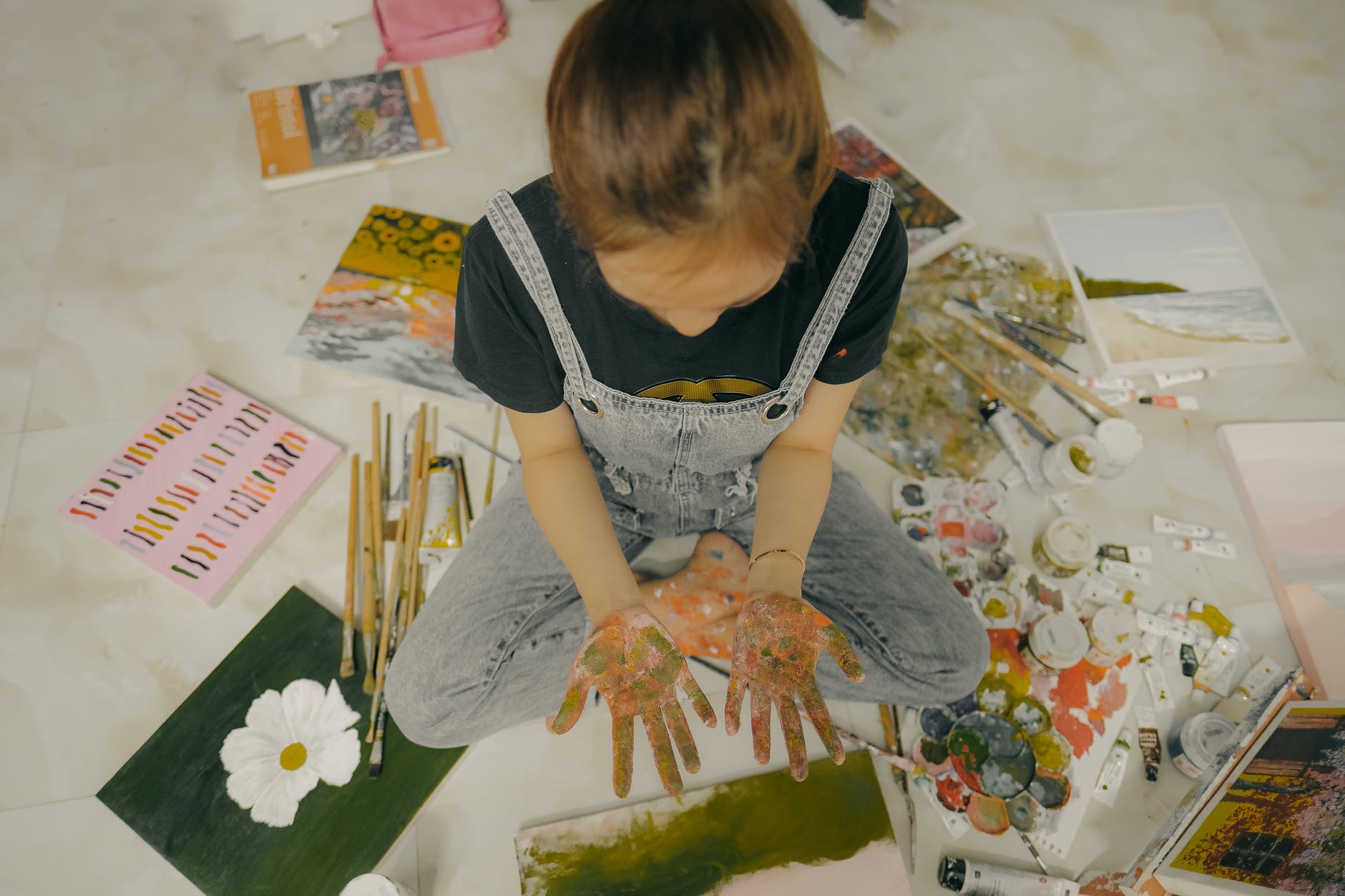 crop unrecognizable girl with hands in paints sitting on floor